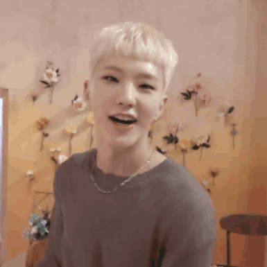 A Man With Blonde Hair Is Smiling In Front Of A Wall With Flowers On It . GIF