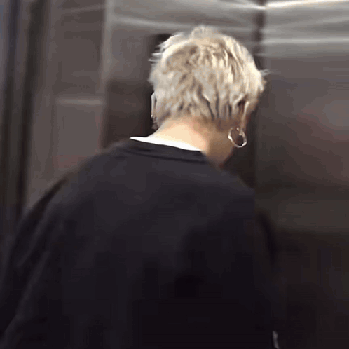 A Man With Blonde Hair Is Standing In An Elevator Wearing Hoop Earrings . GIF