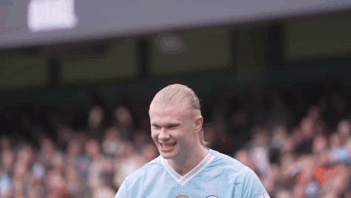 A Man With Blonde Hair Is Wearing A Blue Shirt And Smiling On A Soccer Field . GIF