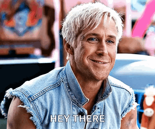 A Man With Blonde Hair Is Wearing A Denim Vest And Smiling While Saying Hey There . GIF