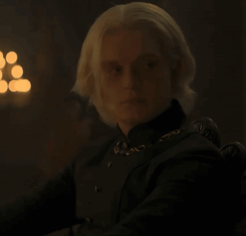 A Man With Blonde Hair Wearing A Black Shirt And A Gold Chain Around His Neck GIF