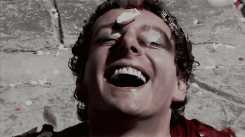 A Man With Blood On His Face Is Laughing With Petals Falling Around Him GIF
