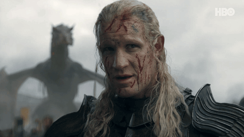 A Man With Blood On His Face Stands In Front Of A Dragon With Hbo Written On The Bottom Right GIF