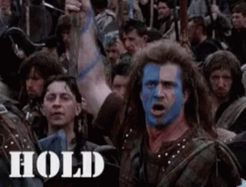 A Man With Blue And White Paint On His Face Is Standing In Front Of A Crowd . GIF