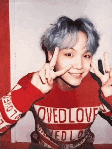 A Man With Blue Hair Is Wearing A Red Sweater And Making A Peace Sign . GIF