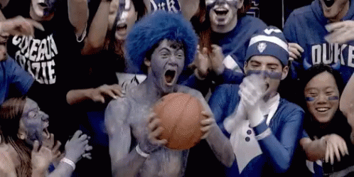 A Man With Blue Paint On His Face Is Holding A Basketball In Front Of A Crowd Of People Wearing Duke Shirts GIF
