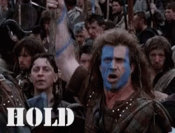 A Man With Blue Paint On His Face Stands In Front Of A Crowd With The Word Hold On The Bottom Right GIF