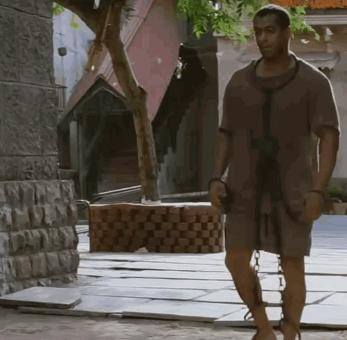 A Man With Chains Around His Legs Is Walking Down A Street GIF