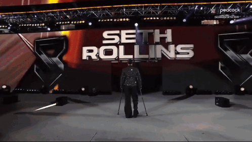 A Man With Crutches Walks On A Stage In Front Of A Sign That Says Seth Rollins GIF