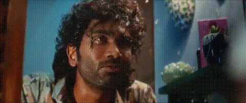 A Man With Curly Hair And A Beard Is Looking At The Camera In A Room . GIF
