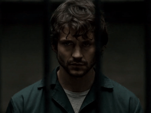 A Man With Curly Hair And A Beard Is Standing In A Dark Room GIF