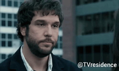 A Man With Curly Hair And A Beard Is Standing In Front Of A Building With The Words @Tvresidence Above Him GIF