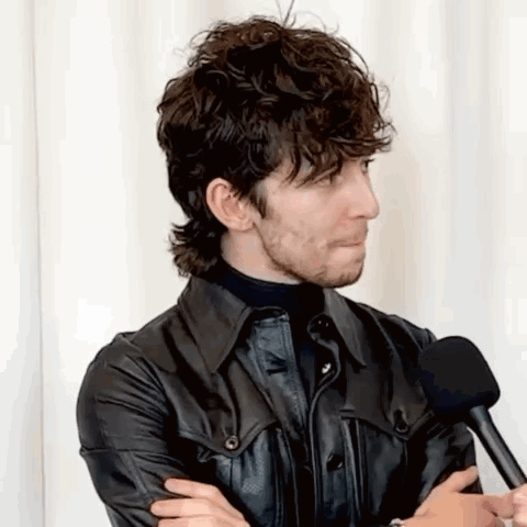 A Man With Curly Hair And A Beard Is Talking Into A Microphone . GIF