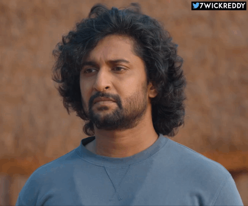 A Man With Curly Hair And A Beard Is Wearing A Blue Shirt With The Hashtag 7Wickreddy GIF