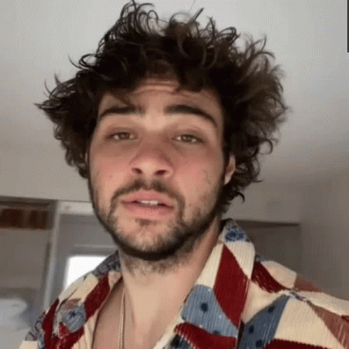 A Man With Curly Hair And A Beard Is Wearing A Colorful Shirt And Making A Funny Face . GIF