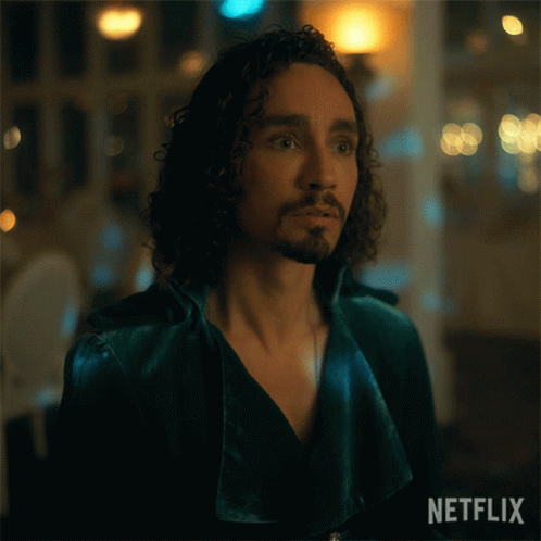 A Man With Curly Hair And A Beard Is Wearing A Green Jacket With Netflix Written On The Bottom GIF