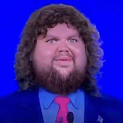 A Man With Curly Hair And A Beard Is Wearing A Pink Tie And A Blue Suit . GIF