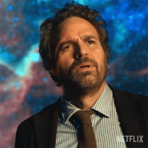 A Man With Curly Hair And A Beard Is Wearing A Suit And Tie And Looking Up At The Sky . GIF