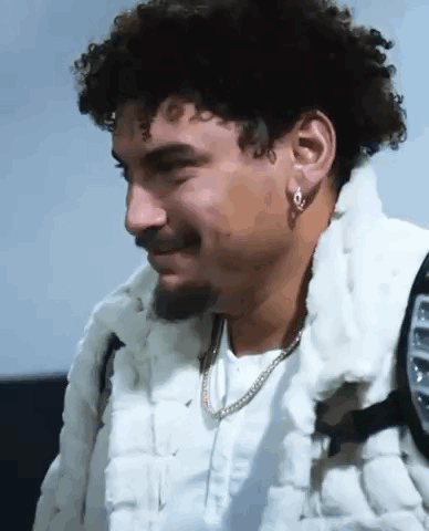 A Man With Curly Hair And A Beard Is Wearing A White Fur Coat . GIF