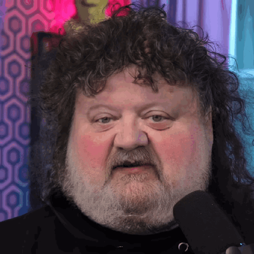 A Man With Curly Hair And A Beard Looks At The Camera GIF