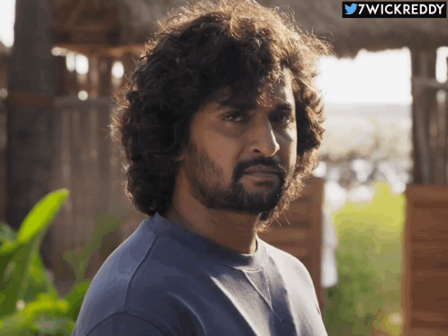 A Man With Curly Hair And A Beard Looks At The Camera With A Twitter Icon Above Him That Says 7Wickreddy GIF