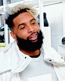 A Man With Curly Hair And A Beard Wearing A White Jacket GIF