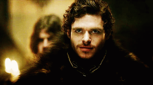 A Man With Curly Hair And A Fur Coat Is Looking At The Camera GIF