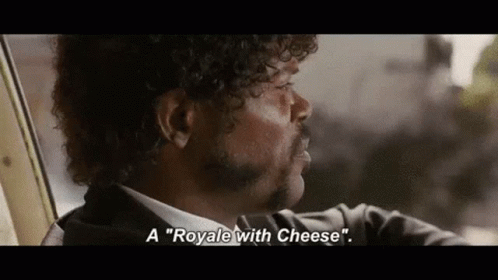 A Man With Curly Hair And A Mustache Is Sitting In A Car And Talking About A Royale With Cheese . GIF
