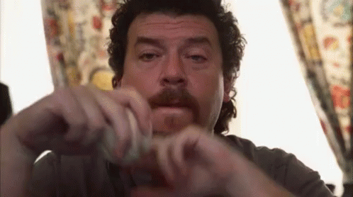 A Man With Curly Hair And A Mustache Is Sitting In Front Of A Window Holding Something In His Hands . GIF