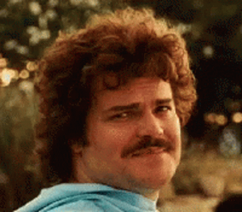A Man With Curly Hair And A Mustache Is Wearing A Blue Sweatshirt And Making A Funny Face . GIF