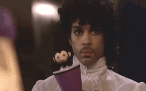 A Man With Curly Hair And A Mustache Is Wearing A Purple Shirt GIF