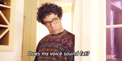 A Man With Curly Hair And Glasses Is Asking Does My Voice Sound Fat GIF