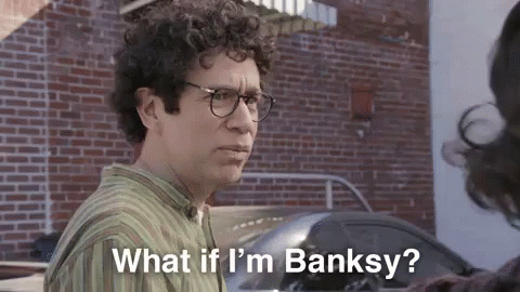 A Man With Curly Hair And Glasses Is Standing In Front Of A Brick Wall And Talking To A Woman . GIF