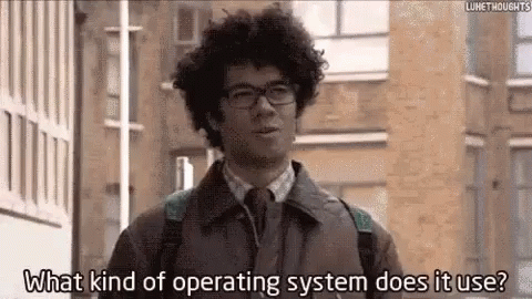 A Man With Curly Hair And Glasses Is Standing In Front Of A Building And Asking What Kind Of Operating System Does It Us GIF