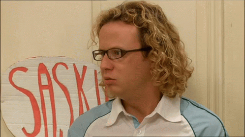 A Man With Curly Hair And Glasses Stands In Front Of A Sign That Says Sas GIF