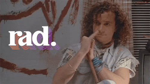 A Man With Curly Hair Has His Finger In His Nose In Front Of A Rad Logo GIF