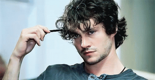 A Man With Curly Hair Is Brushing His Hair With A Comb And Looking At The Camera . GIF