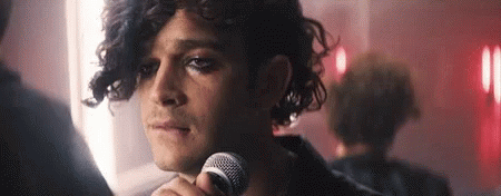 A Man With Curly Hair Is Holding A Microphone In His Hand . GIF