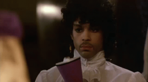 A Man With Curly Hair Is Holding A Purple Cup In His Hand . GIF