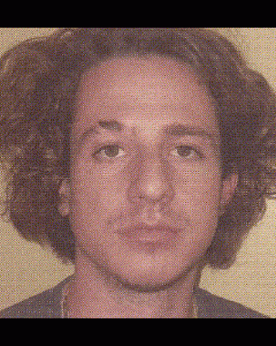 A Man With Curly Hair Is Looking At The Camera With A Blurred Background Behind Him . GIF