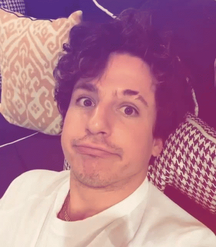A Man With Curly Hair Is Making A Funny Face In Front Of A Patterned Pillow GIF