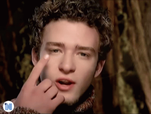 A Man With Curly Hair Is Making A Funny Face With His Finger GIF