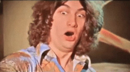A Man With Curly Hair Is Making A Surprised Face With His Mouth Open GIF