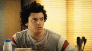A Man With Curly Hair Is Sitting At A Table With A Bottle Of Milk . GIF