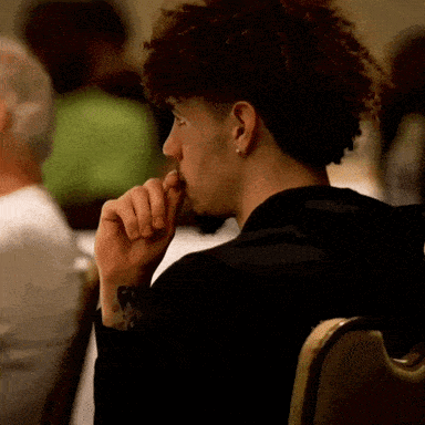 a man with curly hair is sitting in a chair and looking at something