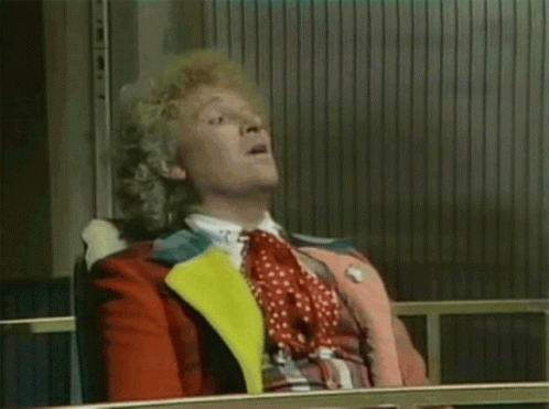 A Man With Curly Hair Is Sitting In A Chair And Making A Funny Face . GIF