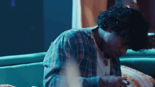 A Man With Curly Hair Is Sitting On A Couch Looking Down GIF