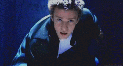 A Man With Curly Hair Is Smiling In Front Of A Blue Wall GIF