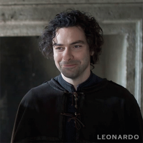 A Man With Curly Hair Is Smiling In Front Of A Leonardo Sign GIF