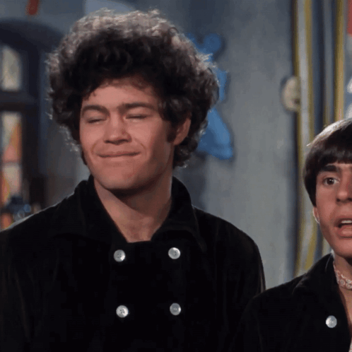 A Man With Curly Hair Is Smiling While Wearing A Black Jacket GIF